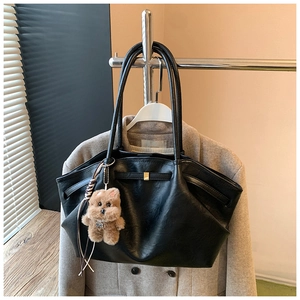 Detail of black pebbled leather tote bag with gold buckle and cute brown bear charm