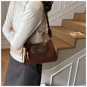 Close-up of brown suede shoulder bag with woven strap and beaded charms in a warm indoor setting