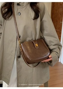 Brown retro PU leather saddle bag with metal buckle shown on a model in a trench coat
