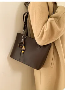 Detail of dark brown leather bucket bag with cute plush pendant and beads on shoulder strap