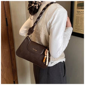 Detail of dark brown retro underarm bag with woven strap and colorful bead charm