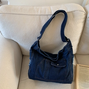 Close-up of a blue denim tote bag with functional pockets and frayed fringe on a sofa