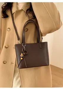 Close-up of a brown PU leather bucket bag with decorative charms on a wool coat