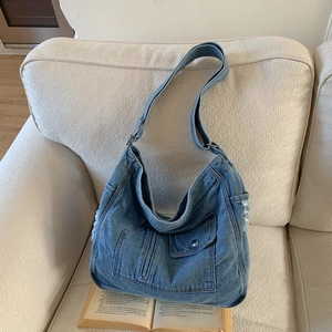 Detail of blue denim hobo bag featuring a flap pocket and vintage frayed edge texture
