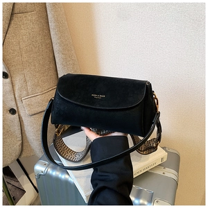 Détail d'un sac à rabat noir avec logo doré et bandoulière tissée dans un cadre de vie