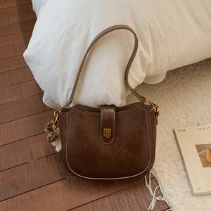 Detail of dark brown vintage shoulder bag featuring a golden clasp and leopard pompom