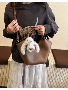 Détail d'un sac seau en cuir grainé marron avec un charm lapin en peluche blanc