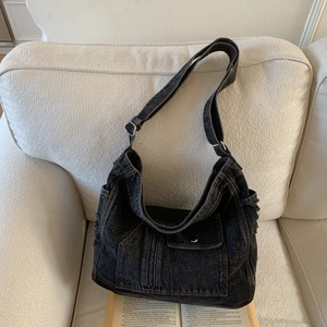 Close-up of black washed denim hobo bag with functional pockets on a textured sofa