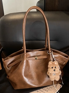 Vintage brown leather tote bag with gold metal buckle and cute plush charm on a sofa
