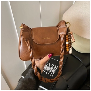 Detail of a brown leather shoulder bag with woven handle and beaded charm accessory