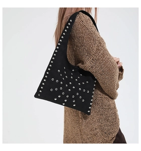 Close-up of black matte suede shoulder bag with decorative silver rivets and wide strap