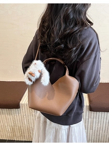 Sac à main en cuir marron avec charme lapin blanc porté à l'épaule par un mannequin