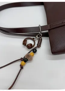 Close-up of a handmade dark brown braided keychain with a mini headphone charm on a leather bag