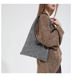 Close-up of grey suede shoulder bag with silver studs on a model wearing brown sweater