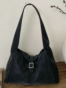 Minimalist black suede hobo shoulder bag with silver buckle and wide strap on wood surface