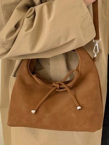 Chic brown suede handbag with decorative knot and silver hardware on a beige trench coat