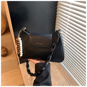 Detail of black crossbody bag with woven strap and beaded pendant charm on wood surface