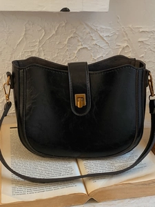 Retro black semi-circle bucket bag with gold buckle on an open book background