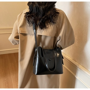 Détail du sac seau en cuir noir avec boucle métallique porté sur un trench-coat beige