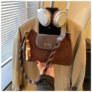 Close-up of deep brown patchwork leather handbag with woven strap and beaded charm details