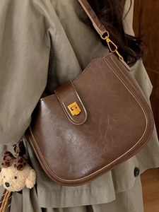 Deep brown leather bucket bag with gold clasp and cute plush bear charm for winter fashion