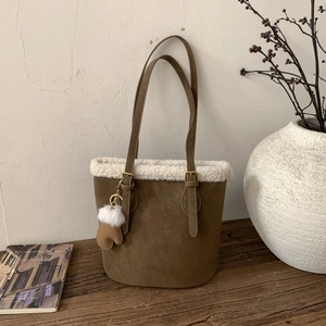 Brown suede bucket bag with white faux fur trim and glove charm on a wooden table