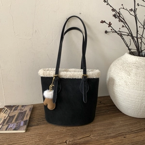 Detail of black suede tote bag with white faux shearling trim and brown glove charm