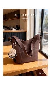 Dettaglio della borsa tote marrone in finta pelle con cuciture bianche e ciondolo a peluche