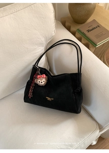 Détail d'un sac cabas en daim noir avec logo doré et pendentif ours en peluche