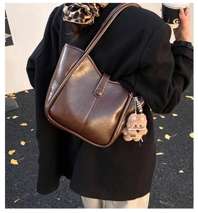 Detail of minimalist dark brown faux leather tote with plush bear charm in autumn setting