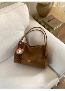 Détail d'un sac cabas en daim marron avec lettrage doré et un charm ours en peluche