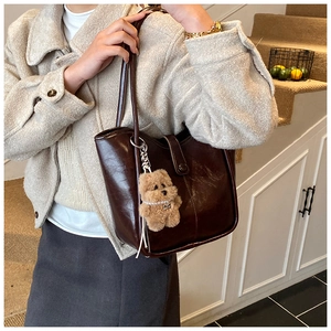 Deep brown faux leather tote bag with a plush bear charm on a model in a warm interior