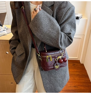 Detail view of burgundy quilted mini box bag with gold chain and cherry charm detail