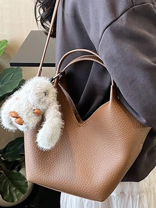 Sac seau en cuir marron avec ouverture en V et breloque lapin en peluche sur un modèle
