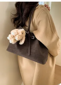 Detail view of large dark brown leather tote bag with a beige plush rabbit charm