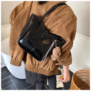 Detail of black glossy leather shoulder bag featuring plush bear and striped ribbon charm