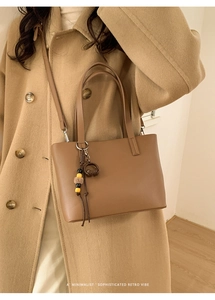 Brown leather bucket bag with top handle and creative headphone pendant on neutral coat