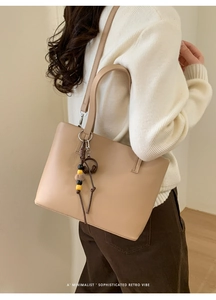 Detail of beige faux leather bucket bag with brown earphone pendant and crossbody strap
