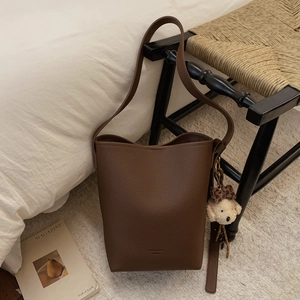 Detailed view of dark brown leather bucket bag with litchi texture and teddy bear charm