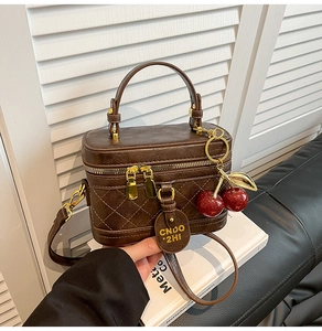 Detailed view of dark brown box bag with quilted texture and cute cherry charm