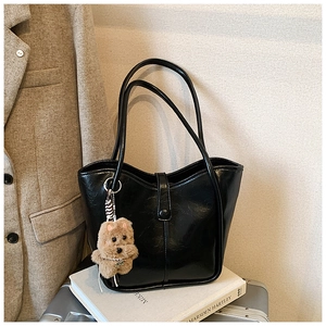 Detail of black faux leather tote bag with glossy finish and brown plush dog charm