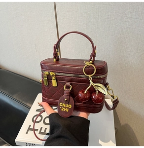 Detail of burgundy quilted box bag featuring cherry charms and elegant gold zipper hardware