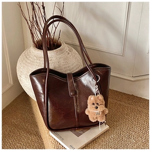 Detailed view of glossy dark brown tote bag with retro buckle and plush bear charm