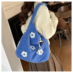 Close-up of blue plush tote bag featuring soft white floral embroidery and drawstring tie