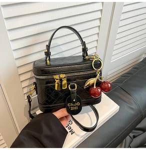 Detail of black quilted box handbag with gold zippers and a red sequin cherry charm