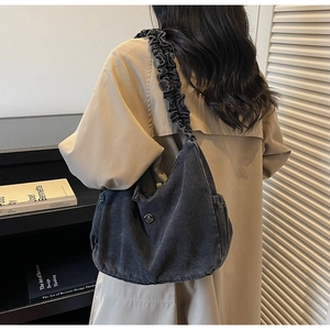 Detail view of dark grey denim shoulder bag with pleated strap and metal M logo on a model