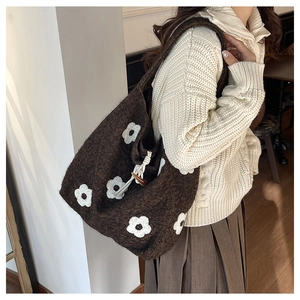 Detail of dark brown knit tote bag showing white daisy flower embroidery and horn button closure