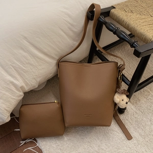Brown leather bucket bag set with small pouch and bear charm in a cozy indoor setting