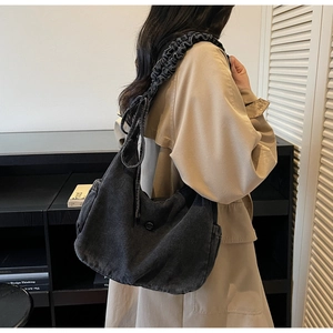 Detail of black washed denim hobo bag with wide pleated strap worn over a khaki coat