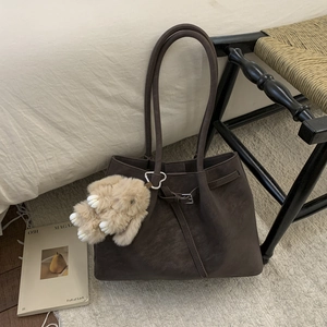 Detail of dark brown tote bag with suede texture and cute plush bunny charm accessory